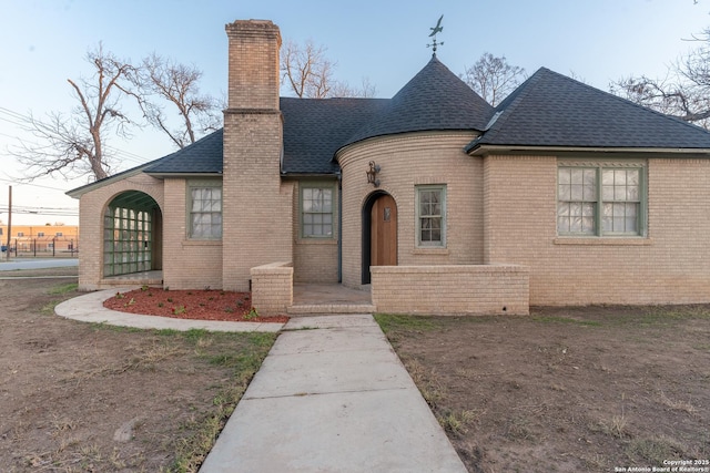 view of front of property with a shingled roof, brick siding, and a chimney