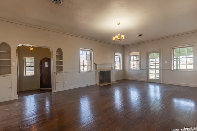 unfurnished living room featuring arched walkways, a notable chandelier, dark wood finished floors, and plenty of natural light