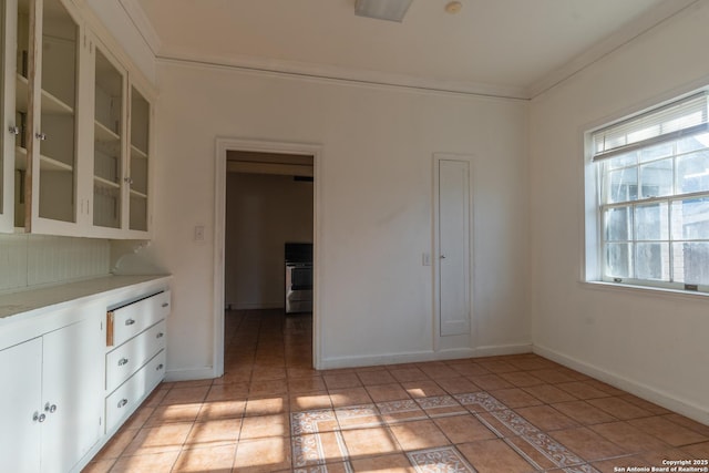 interior space with light tile patterned floors, baseboards, light countertops, glass insert cabinets, and crown molding