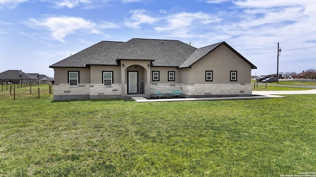 view of front of property with stone siding, fence, a front lawn, roof with shingles, and stucco siding