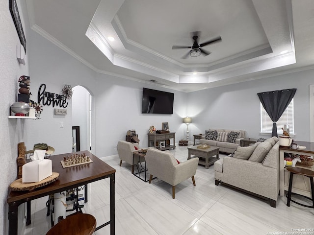 living area featuring a ceiling fan, a raised ceiling, arched walkways, and crown molding