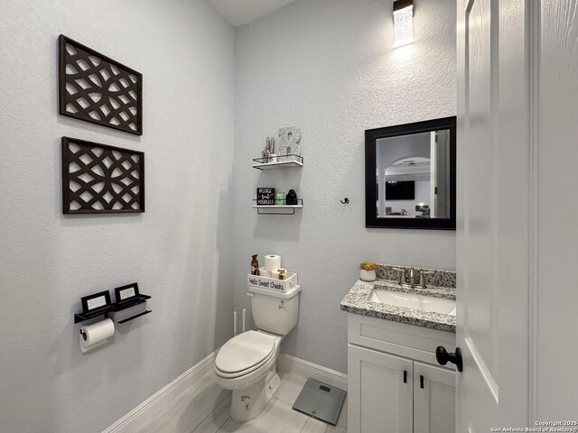 half bath with baseboards, toilet, and vanity