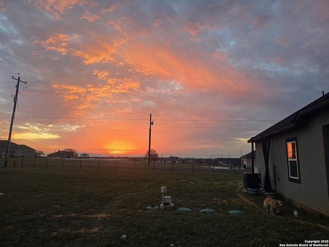 yard at dusk featuring cooling unit and fence