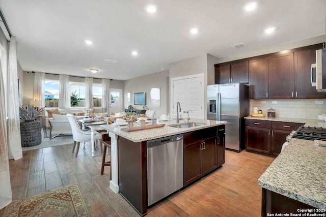 5718 Agate Cir, San Antonio, TX 78222 - kitchen featuring dark brown cabinets, backsplash, an island with sink, stainless steel appliances, and a sink