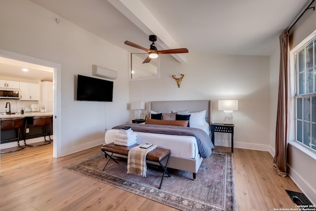 bedroom featuring lofted ceiling with beams, light wood-style floors, baseboards, and a sink