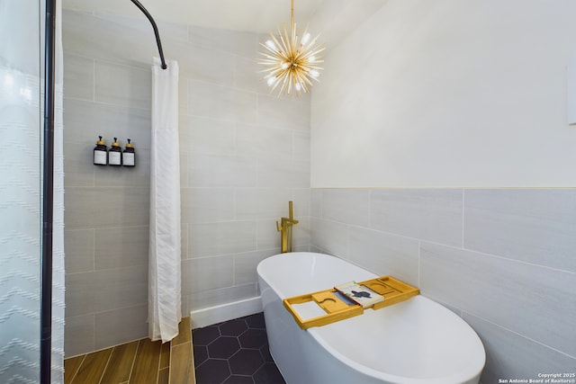 full bath featuring tile patterned floors, a tile shower, tile walls, an inviting chandelier, and a freestanding bath