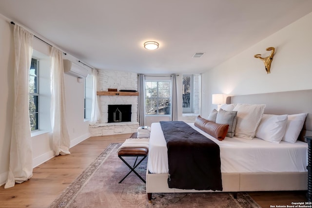 bedroom featuring visible vents, an AC wall unit, wood finished floors, a fireplace, and baseboards