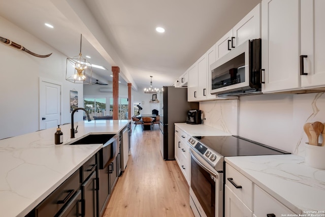 kitchen with a sink, hanging light fixtures, appliances with stainless steel finishes, white cabinetry, and a notable chandelier