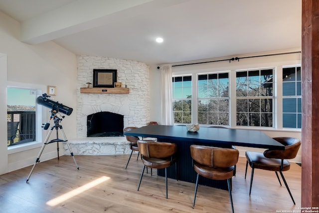 dining space featuring a stone fireplace, vaulted ceiling with beams, baseboards, and wood finished floors