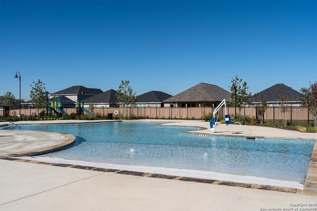 community pool with a patio area, a playground, and fence