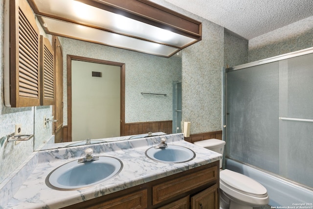 10103 Northampton, San Antonio, TX 78230 - bathroom featuring toilet, double vanity, a textured ceiling, shower / bath combination with glass door, and wallpapered walls