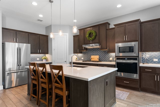 kitchen with visible vents, dark brown cabinets, under cabinet range hood, appliances with stainless steel finishes, and a sink