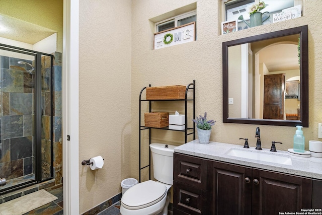 full bath featuring a stall shower, toilet, a textured wall, and vanity