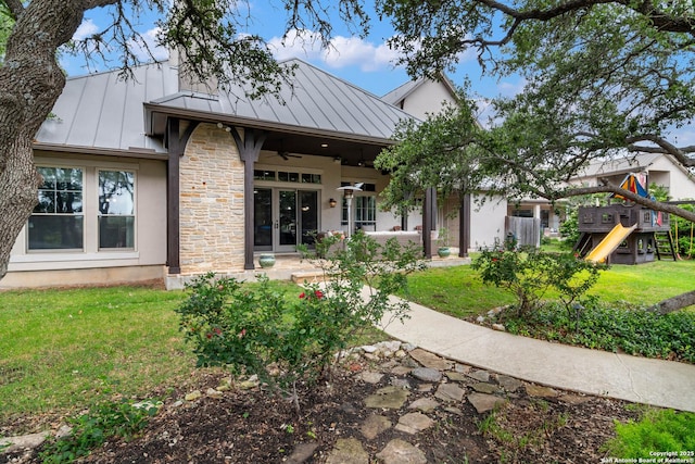 back of property with a standing seam roof, a ceiling fan, a yard, and metal roof
