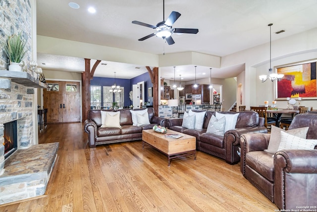 living room featuring visible vents, ceiling fan with notable chandelier, a stone fireplace, and light wood finished floors