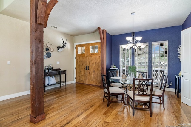dining area with a textured ceiling, a notable chandelier, baseboards, and light wood-style floors