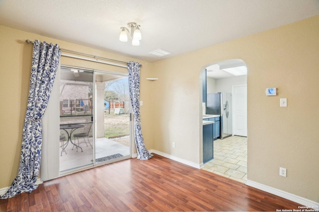 empty room featuring visible vents, baseboards, arched walkways, and wood finished floors