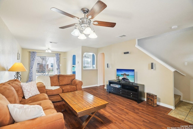 living area with arched walkways, ceiling fan, visible vents, and stairs