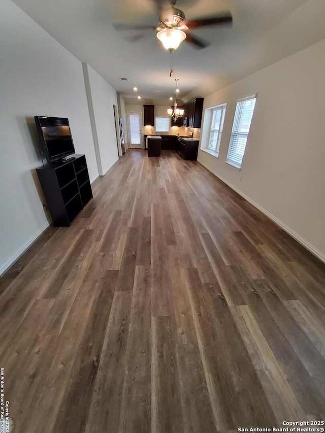 1976 Cowan Dr, New Braunfels, TX 78132 - unfurnished living room featuring baseboards, dark wood finished floors, and ceiling fan with notable chandelier