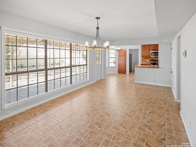 unfurnished dining area with a chandelier, brick floor, and baseboards