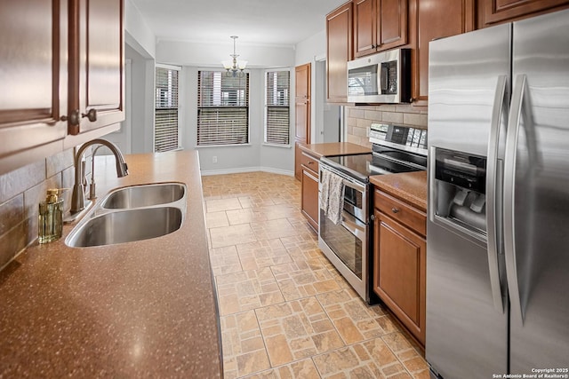 kitchen featuring a notable chandelier, stone finish floor, a sink, backsplash, and stainless steel appliances