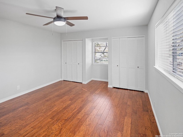 unfurnished bedroom featuring ceiling fan, baseboards, multiple closets, and wood finished floors