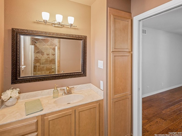 full bathroom with visible vents, wood finished floors, a tile shower, baseboards, and vanity