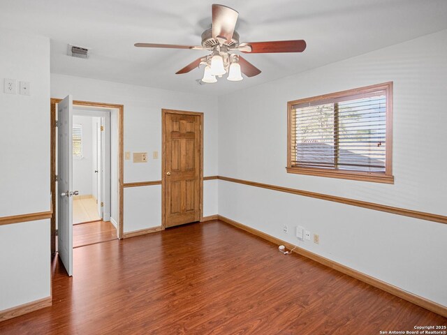 spare room featuring a ceiling fan, visible vents, dark wood-style flooring, and baseboards