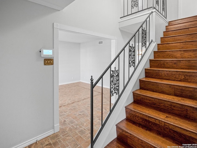 stairs with visible vents, brick floor, a high ceiling, and baseboards