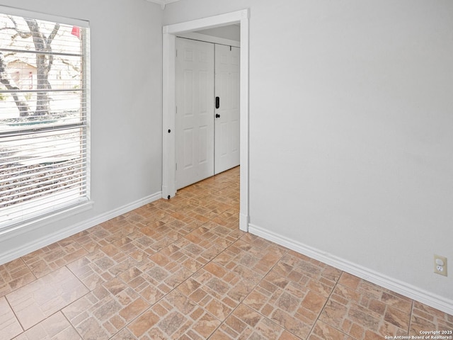 empty room with brick floor, baseboards, and plenty of natural light