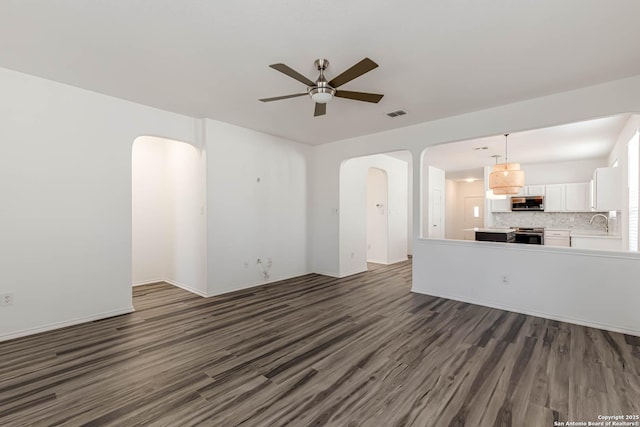 7519 Paraiso Hvn, Boerne, TX 78015 - unfurnished living room featuring visible vents, dark wood finished floors, arched walkways, a ceiling fan, and a sink