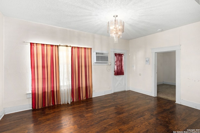spare room featuring a textured ceiling, a wall mounted AC, an inviting chandelier, and wood finished floors