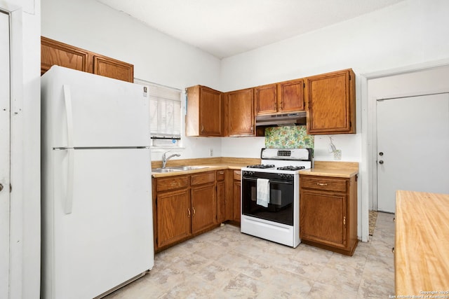kitchen with freestanding refrigerator, a sink, light countertops, under cabinet range hood, and gas range