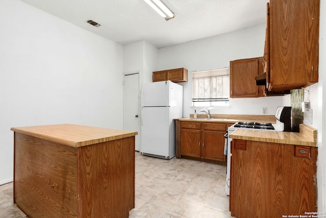 kitchen with a sink, white appliances, brown cabinetry, and butcher block counters