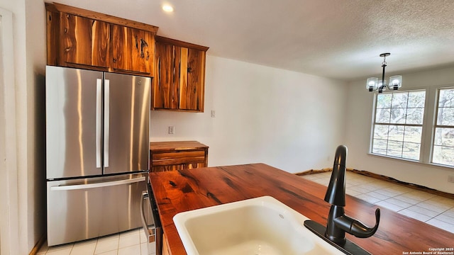 kitchen featuring a sink, a textured ceiling, freestanding refrigerator, brown cabinetry, and light tile patterned floors