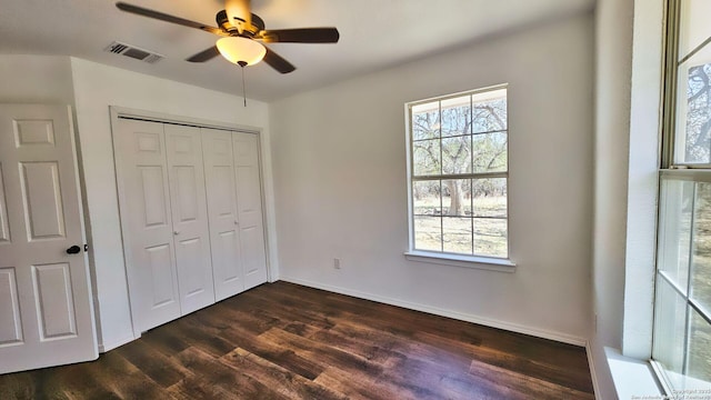 unfurnished bedroom featuring dark wood-type flooring, multiple windows, visible vents, and a closet