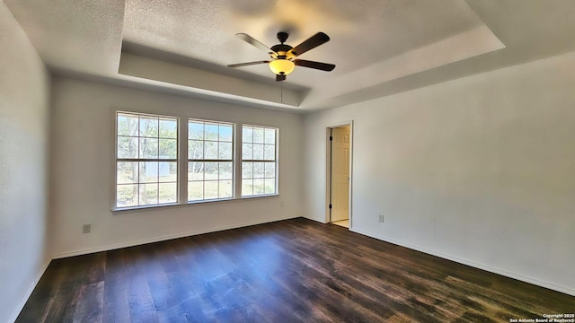 empty room featuring a raised ceiling, a textured ceiling, baseboards, ceiling fan, and dark wood-style flooring