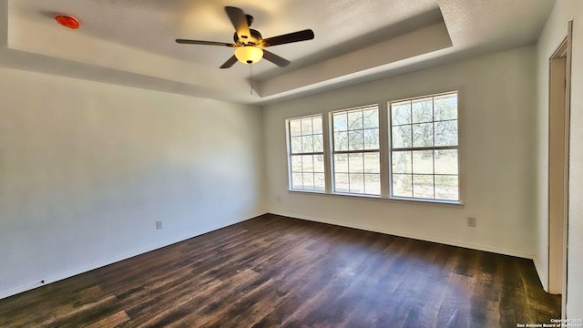 unfurnished room featuring baseboards, a tray ceiling, a textured ceiling, a ceiling fan, and dark wood-style flooring
