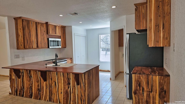 kitchen with brown cabinetry, appliances with stainless steel finishes, a textured ceiling, and a peninsula