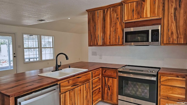 kitchen featuring visible vents, butcher block counters, a peninsula, stainless steel appliances, and a sink