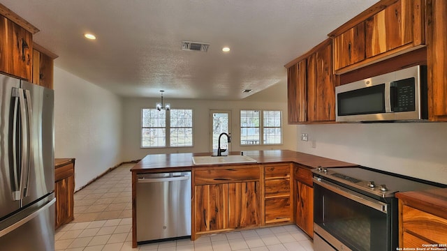 kitchen featuring a sink, stainless steel appliances, a peninsula, brown cabinetry, and a chandelier