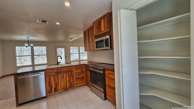 kitchen featuring brown cabinetry, visible vents, a peninsula, a sink, and stainless steel appliances
