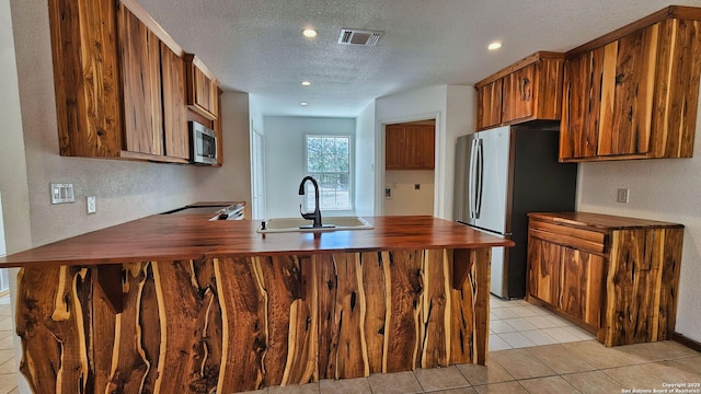 kitchen featuring visible vents, a peninsula, butcher block countertops, a sink, and appliances with stainless steel finishes
