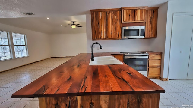 kitchen with light tile patterned floors, brown cabinetry, visible vents, a sink, and stainless steel appliances