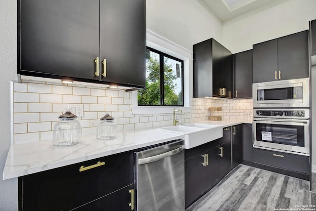 kitchen with appliances with stainless steel finishes, a sink, dark cabinets, and light wood-style flooring
