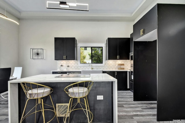 kitchen with dark cabinets, a sink, light wood-type flooring, a kitchen breakfast bar, and backsplash