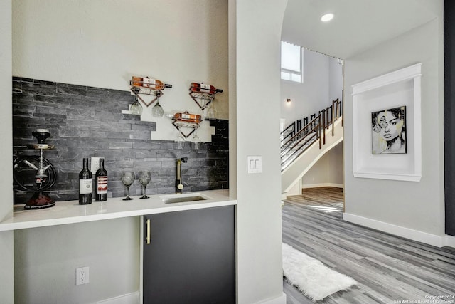 indoor wet bar with decorative backsplash, stairs, arched walkways, wood finished floors, and baseboards