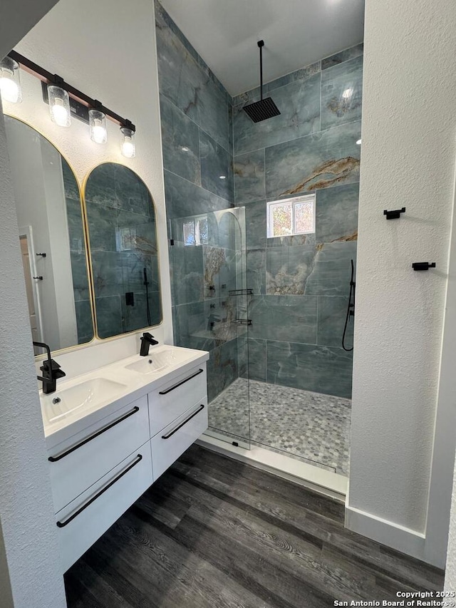 bathroom featuring wood finished floors, a tile shower, and double vanity