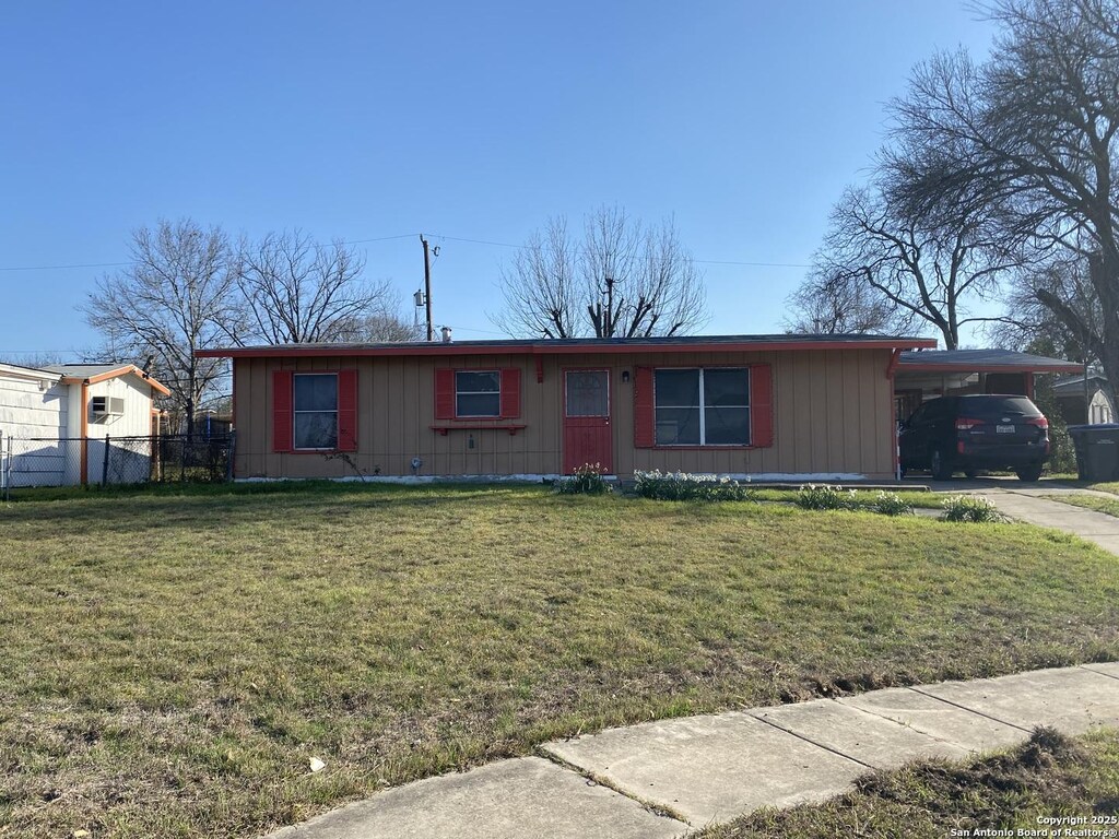 ranch-style home featuring driveway, a front lawn, fence, board and batten siding, and an attached carport