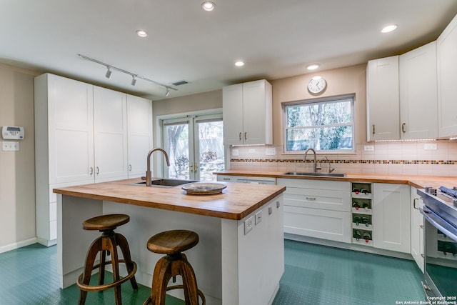 kitchen featuring butcher block countertops, gas range, a breakfast bar area, decorative backsplash, and a sink